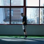 Young man exercising with a skipping rope in an urban gym with large windows and city view.